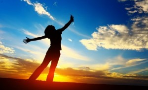 Young woman with raised hands standing on meadow on sunset